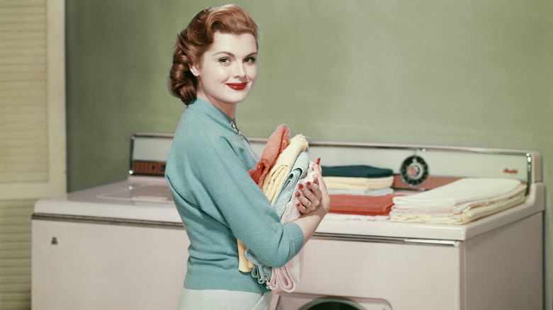 A smiling woman holding a stack of folded towels in front of a 1950s washer-and-dryer combo.