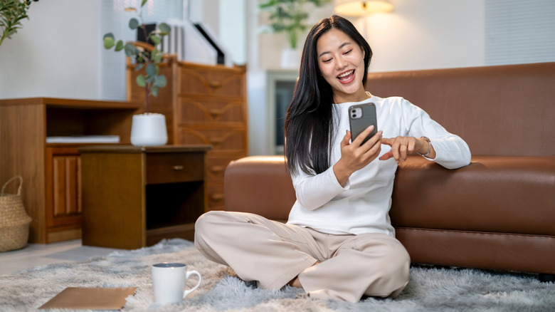 A woman smiling while sitting on the floor and browsing her phone