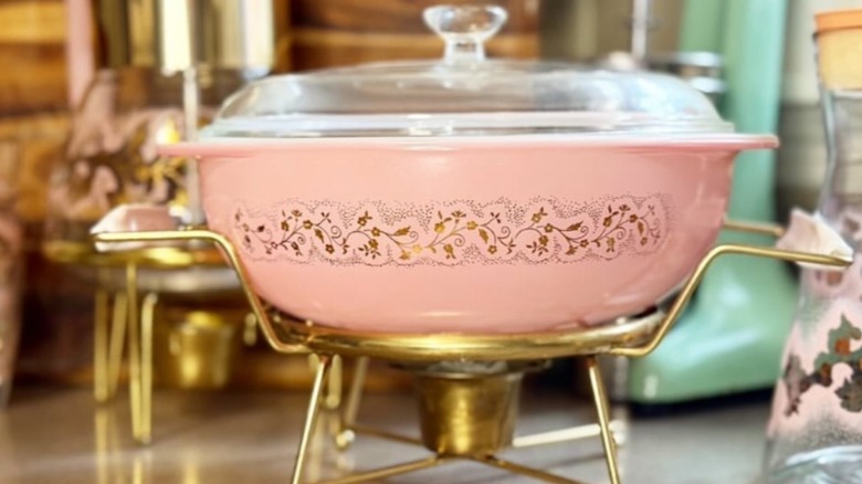A vintage Pyrex Pink Duchess casserole dish on a golden metal stand.