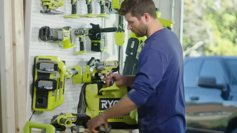 Man putting drill in tool bag, with other Ryobi tools hanging on peg board
