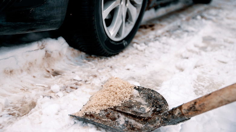 snowy driveway with a car and a shovel removing snow and ice