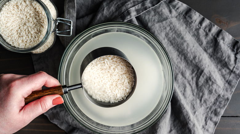 A bowl of rice water on a gray napkin with a scoop full of white rice.
