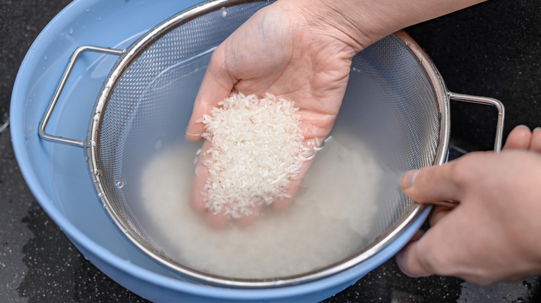 Close-up of a hand rinsing white rice in a colander and collecting liquid in a blue bowl.
