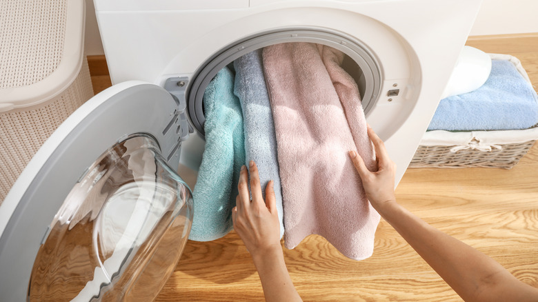 hands putting blue, purple, and pink towels into a white front-loading washer