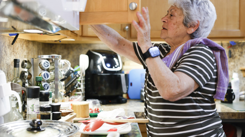 An old woman is looking inside her kitchen cabinets