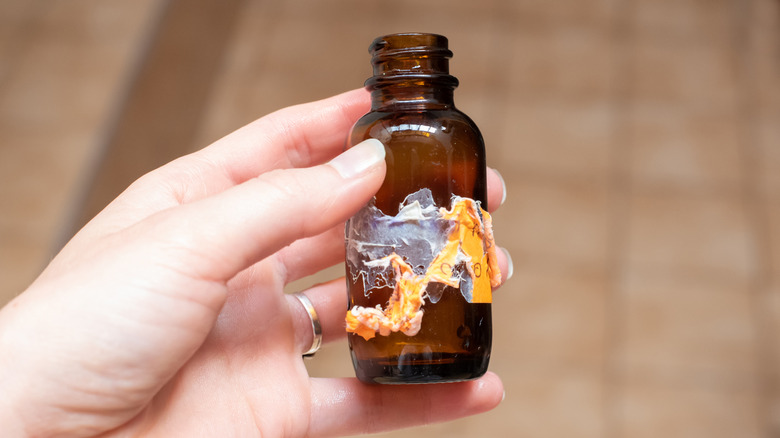 Person holding brown bottle with sticker residue