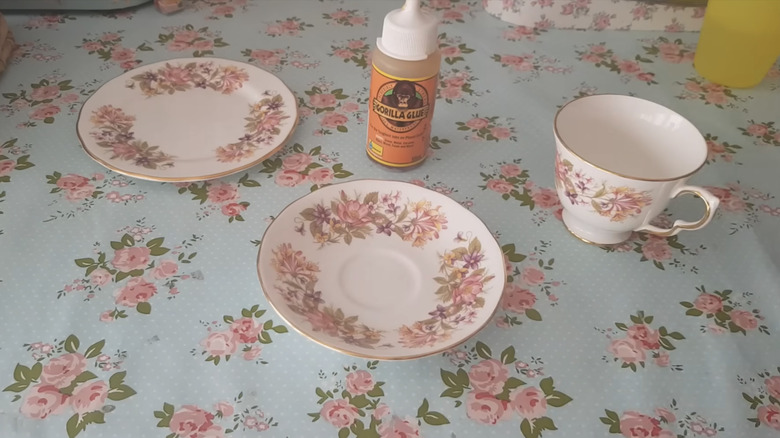 A teacup and two saucers with a bottle of Gorilla Glue on a table with a floral table cloth