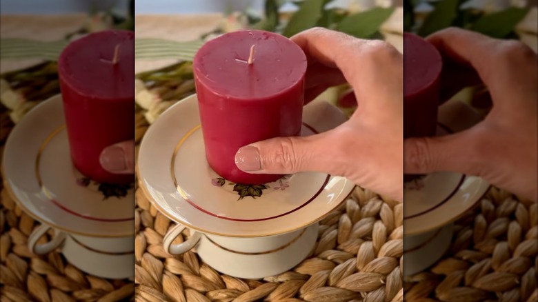 A person's hand setting a red candle on a teacup holder