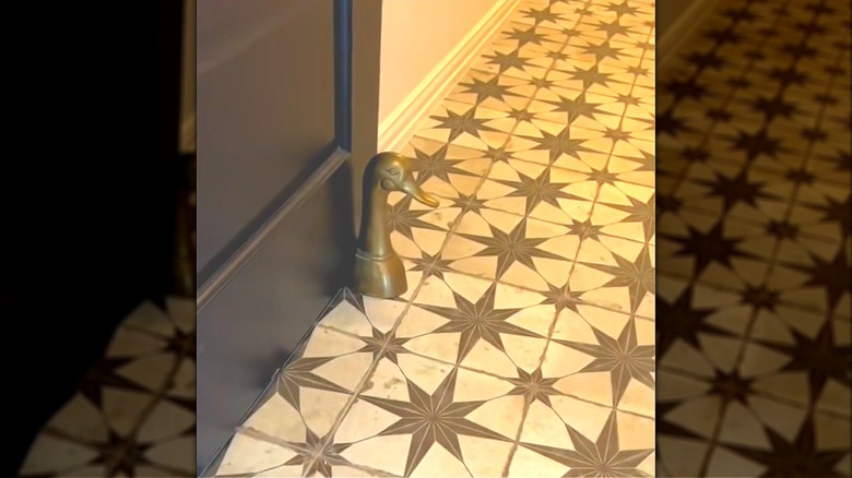 Vintage brass goose bookend used as doorstop on classic tile floor against brown door.