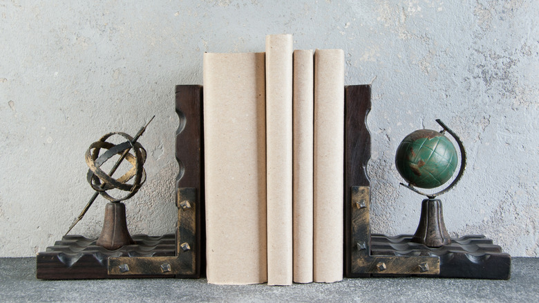 Aged metal bookend statues on either side of beige books on stone background.