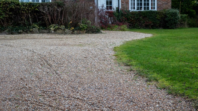 A gravel driveway and parking area in front of an older brick house