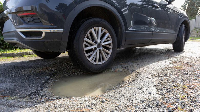 A car tire next to a hole in a gravel driveway with standing water in it