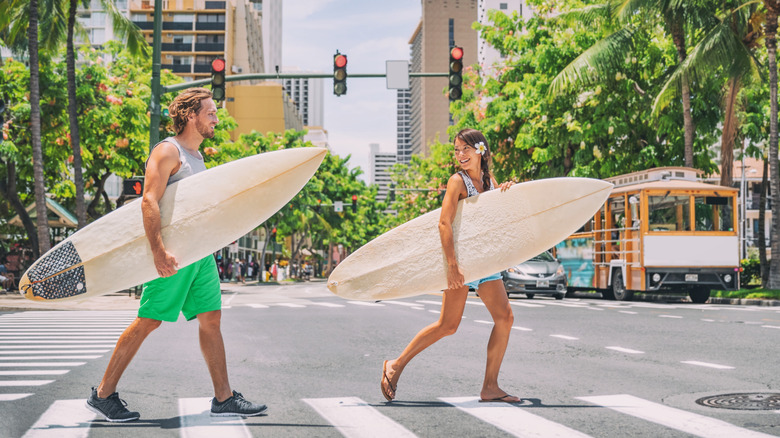 man and woman hilding surf boards cross the road at a stoplight in Hawaii