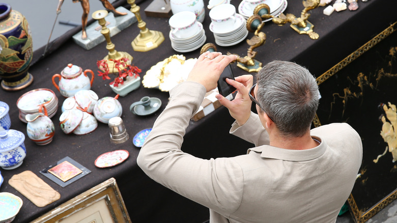 A man takes a photo of dishware at an antique market