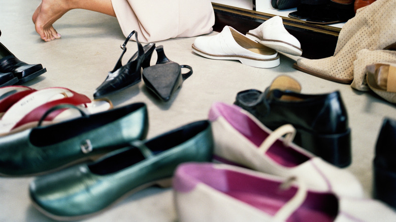 woman kneeling in her closet to look for a pair of shoes while a messy pile of shoes sits on the floor beside her