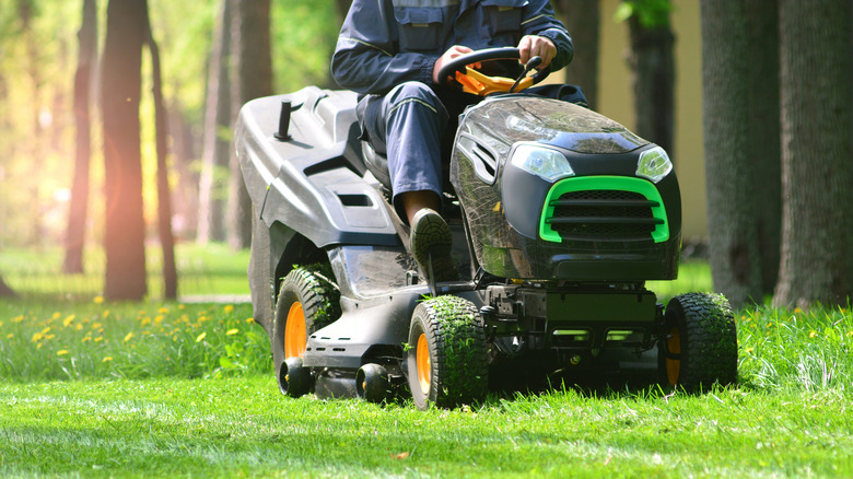 A person sitting in a lawn mower, mowing a green lawn.
