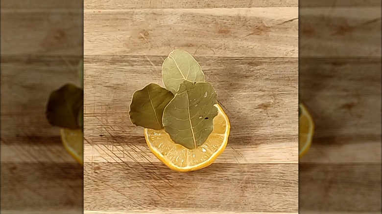 a sliced lemon with three bay leaves stuck in it on top of a wooden surface