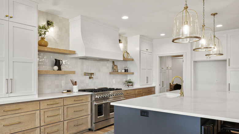 A modern kitchen with a brass and glass lighting over the island, pot lights, and wall sconces