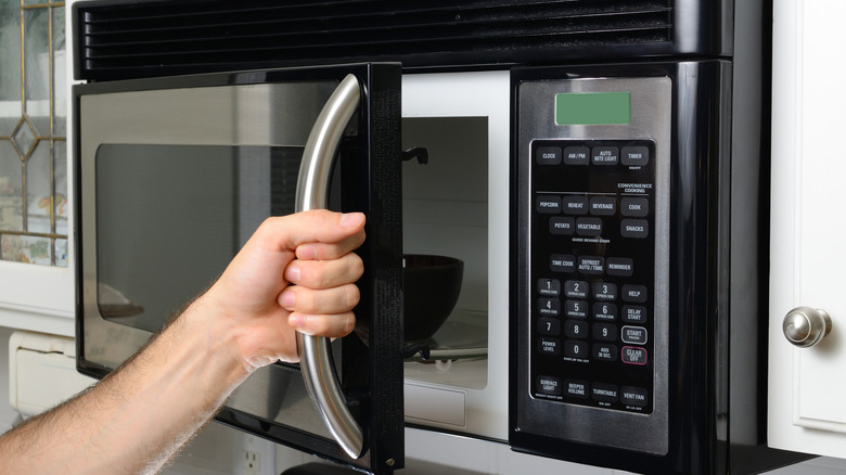 Hand holding handle to open a microwave oven