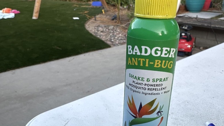 A close-up of Badger Anti-Bug spray bottle, with a residential yard in the background.