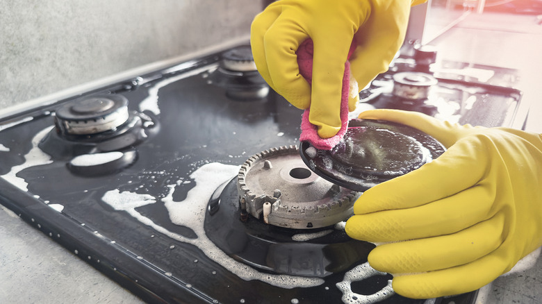 wearing rubber gloves and cleaning a gas stovetop