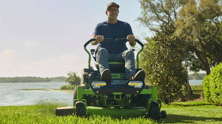 A man smiles while using a Greenworks Crossover Zero Turn mower in front of a white house