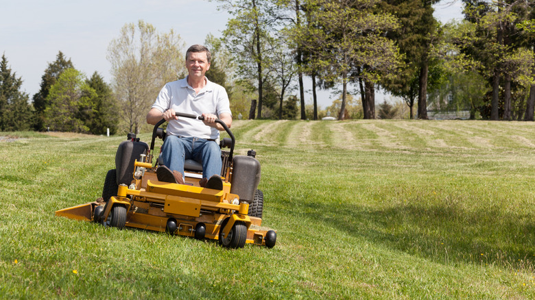 A middle-aged man smiles while using a zero-turn mower to cut a large grassy field