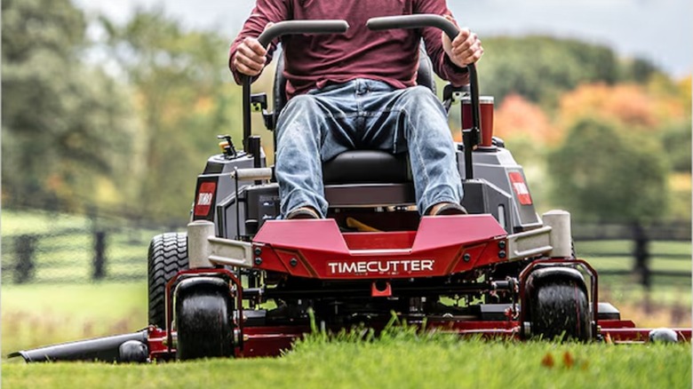 A person rides a Toro TimeCutter Zero-turn riding lawn mower in front of a fenced pasture