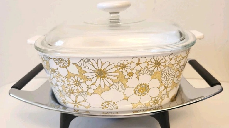 A Corningware Floral Bouquet casserole with lid and stand.