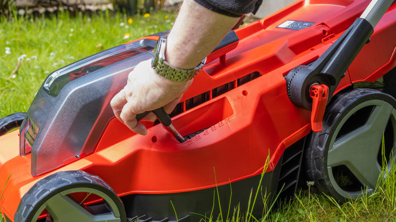 Hand adjusting the height of a red lawn mower