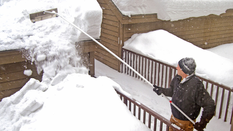 Man with a snow rake removing ice and snow from roof