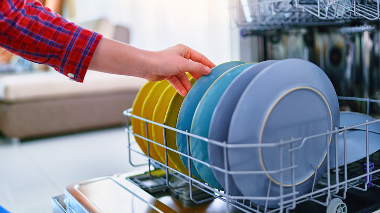 Person loading colorful dishes into dishwasher