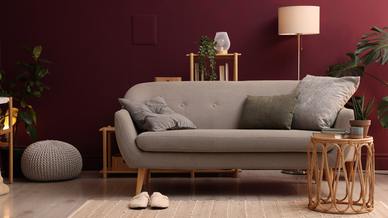 A taupe sofa and warm wood furniture artfully arranged in a burgundy living room