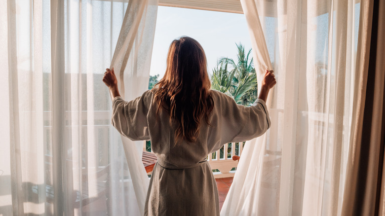 woman opening flowing white sheer drapery on a door to a balcony