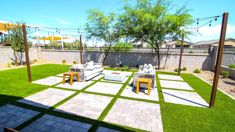 An outdoor seating area in bright sunshine with wicker furniture on concrete pads, with string lights.