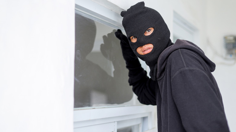 A man wearing a mask looking in a curtained window of a home