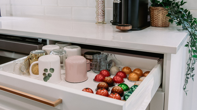 Coffee mugs and pods in a white kitchen drawer