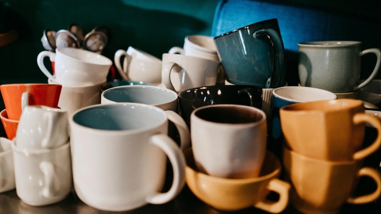A pile of multi-colored ceramic mugs stacked on top of one another in a cabinet