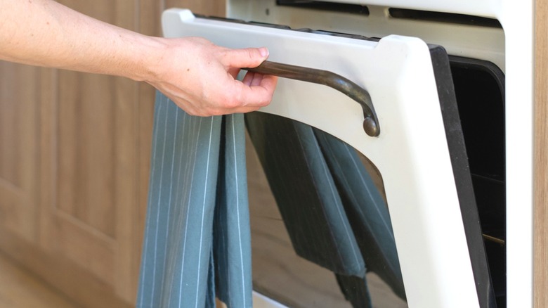 Person opening oven door with kitchen towel on the door handle