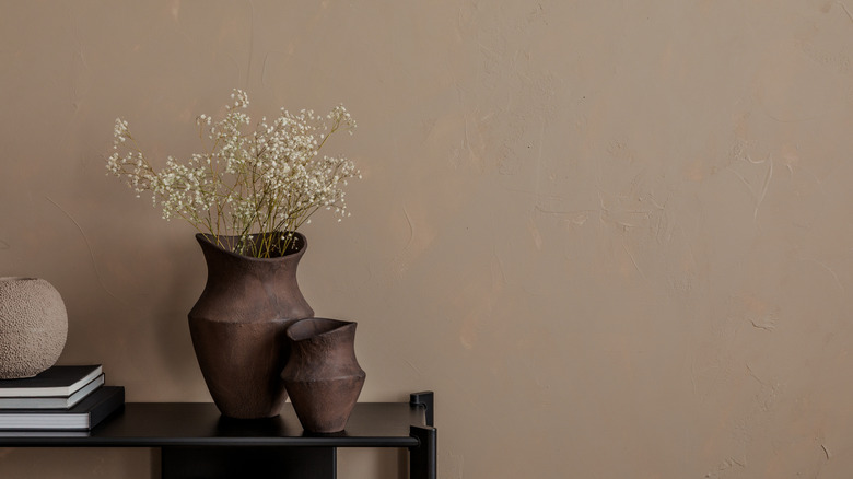 A wall painted in taupe color with a shelf and two flower vases