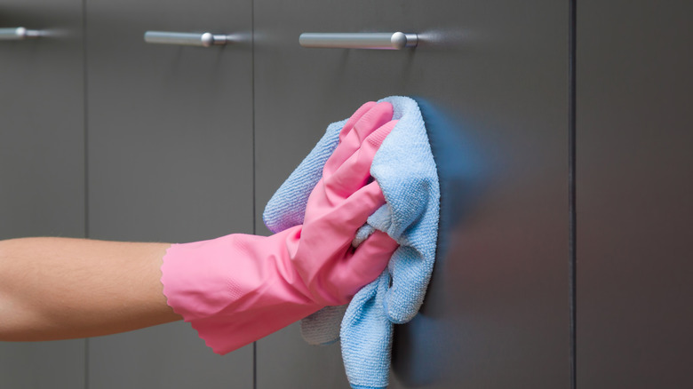 closeup of gloved hand wiping down cabinets