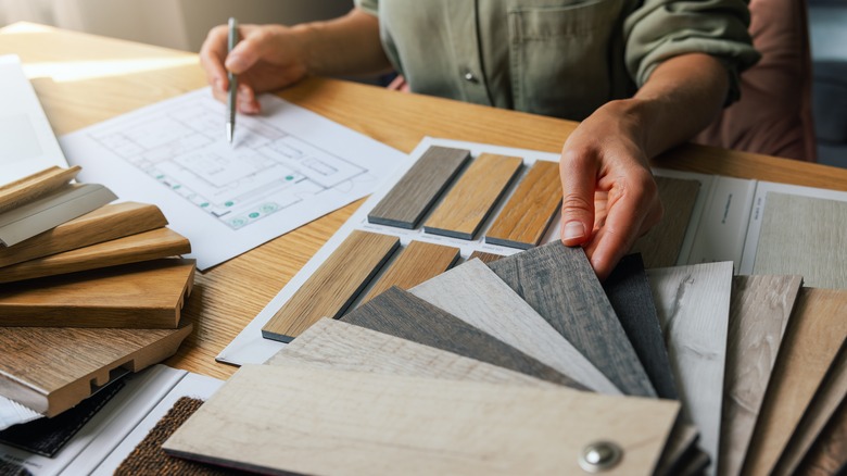 a person looking through potential wood flooring sample options and referencing a floor plan on the desk next to the samples