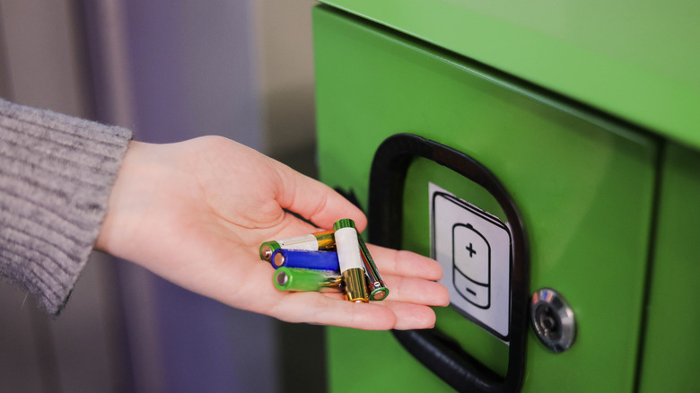 A hand placing several batteries into a recycling receptacle