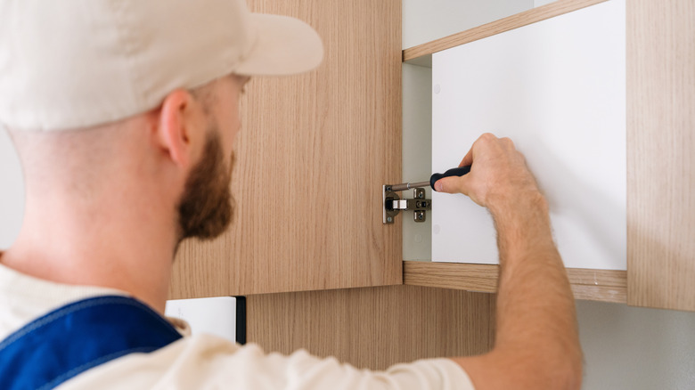 Man screwing interior hinges of kitchen cabinet