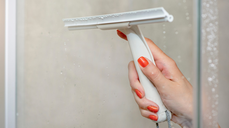 a hand cleaning a shower door with a squeegee