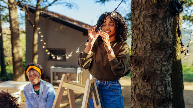 A young Black woman sets up outdoor string lights