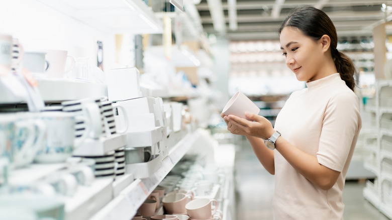 A woman looking at mugs in a thrift shop.