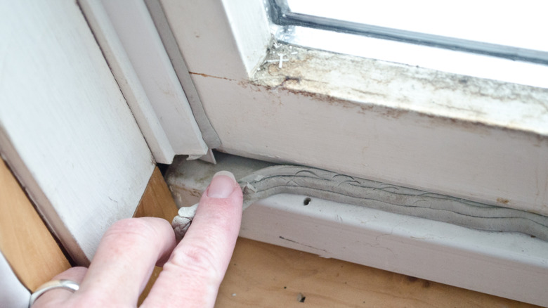 A woman's hand uses gray caulk to seal a window casing