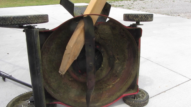 a push lawn mower sitting on its side with a board edged by the blade