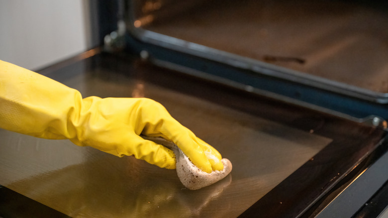 A gloved hand cleaning the glass of a dirty oven